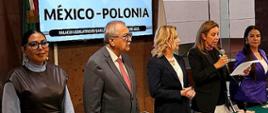 En la foto se ve a cinco personas de pie en fila, de frente a la cámara.
De izquierda a derecha: la diputada Genoveva Huerta Villegas, el diputado Pedro Vázquez González, la embajadora de la República de Polonia Agnieszka Frydrychowicz-Tekieli, la diputada María Angélica Granados Trespalacios y la diputada Alma Lidia De la Vega Sánchez.
Todos visten de manera elegante, con trajes o vestidos formales. Los participantes tienen expresiones tranquilas y concentradas, y algunos sonríen levemente. Al fondo se ve la sala del Parlamento con los emblemas y banderas de México, lo que le da a la escena un carácter solemne y oficial.
La foto muestra el momento de la declaración de la instalación del Grupo de Amistad México-Polonia por parte de la presidenta del grupo.