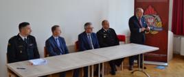 Zdjęcie przedstawia przemawiającego Posła na Sejm RP Zbigniewa Chmielowca oraz prezydium w osobach od lewej: st. bryg. Witolda Wierciocha w umundurowaniu wyjściowym, Zastępcę Prezesa Zarządu WFOŚiGW w Rzeszowie Bogusława Kidę, Posła na Sejm RP Kazimierza Moskala oraz Starostę Powiatu Ropczycko-Sędziszowskiego Witolda Darłaka w mundurze wyjściowym OSP.