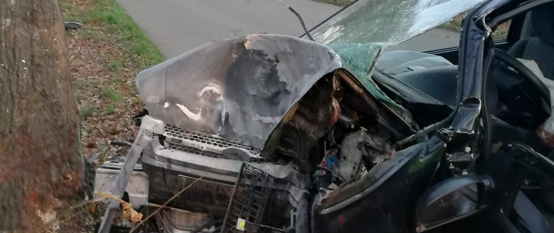 Samochód osobowy uderzył w drzewo, .ma rozbity przód, wybitą szybę przednią i otwarte drzwi od strony kierowcy. 