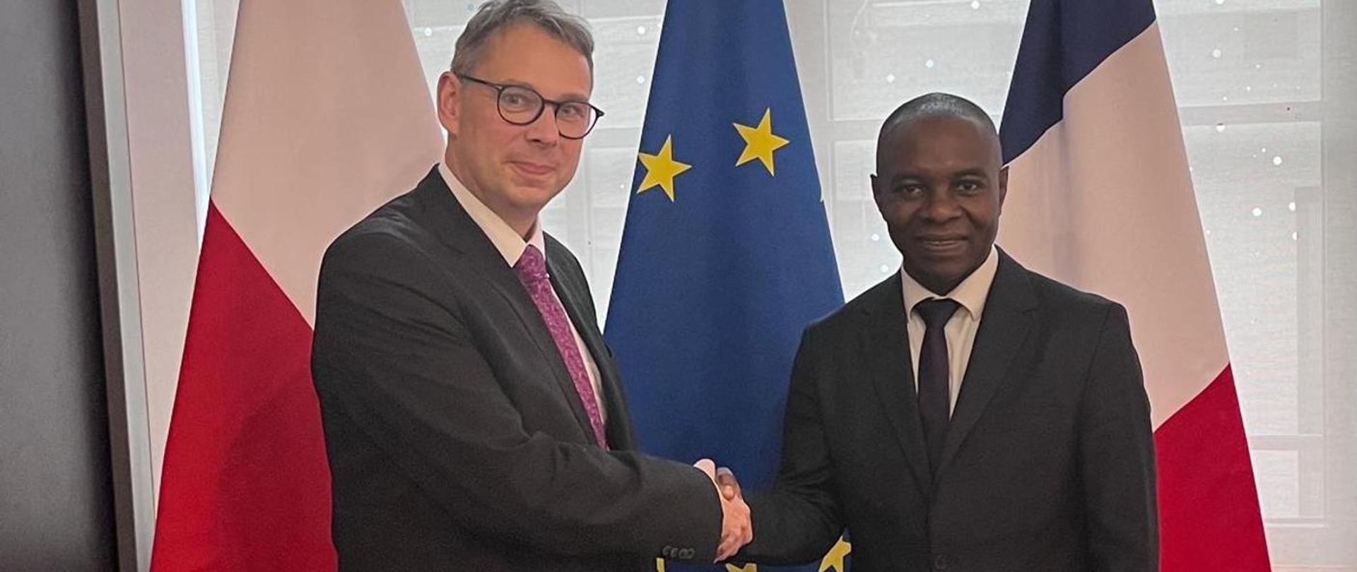 Dwóch mężczyzna w garniturach pozują do zdjęcia i podają sobie rękę