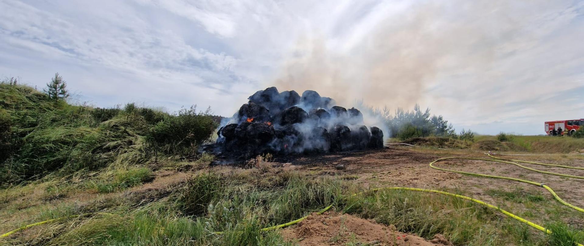 Widać palący się stóg balotów słomy, po lewej zielona trawa