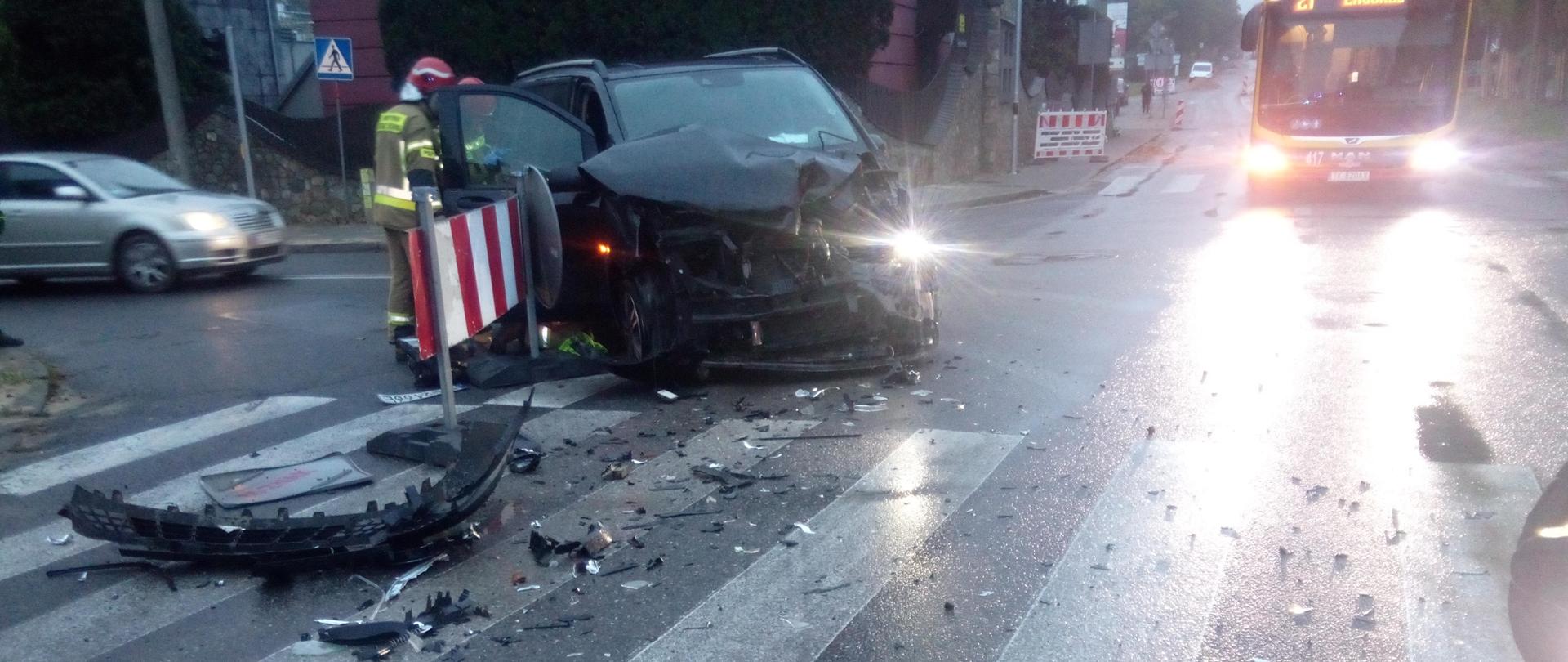 Zdjęcie przedstawia samochód osobowy po kolizji stojący na ulicy Zagórskiej. Przed nim rozrzucone fragmenty karoserii, a przy aucie stoi ratownik. 