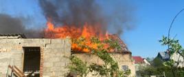 W centralnej części widać budynek gospodarczy, którego dach w całości objęty jest pożarem.