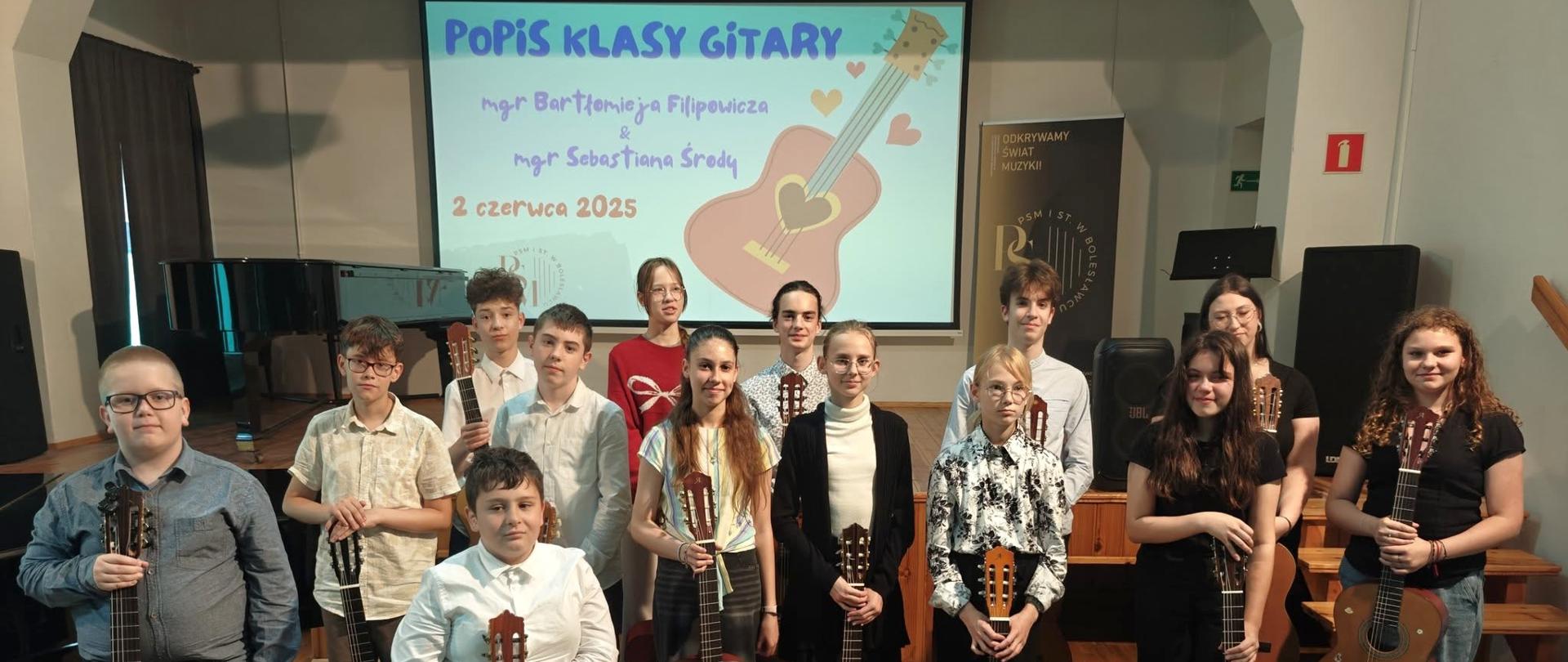 Zdjęcie przedstawiające wykonawców popisu klasy gitary mgr Bartłomieja Filipowicza i mgr Sebastiana Środy, który odbył się 2 czerwca 2025 roku w auli szkoły.