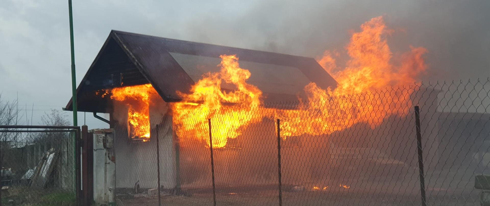 Budynek mieszkalny z którego okinen wydobywalą się płomienie.