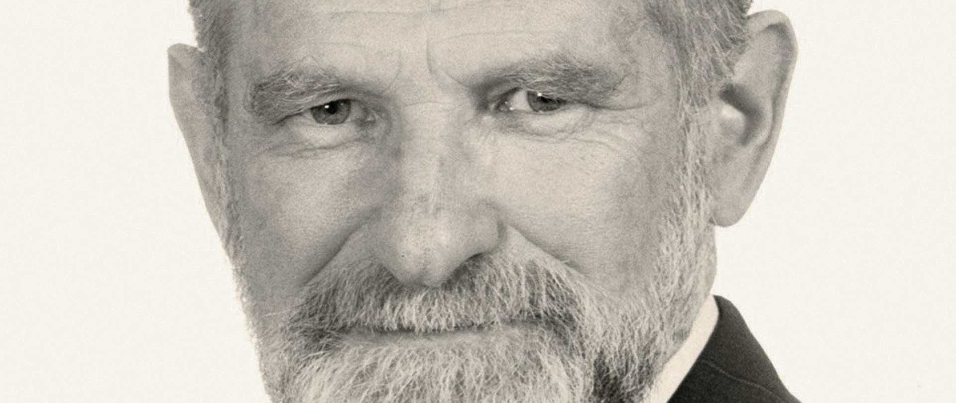 Bronisław Geremek - czarno - biały portret mężczyzny, siwe włosy, broda, ciemna marynarka w paski, krawat w paski, biała koszula.