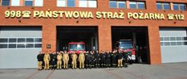 Strażacy stoją na tle budynku komendy PSP