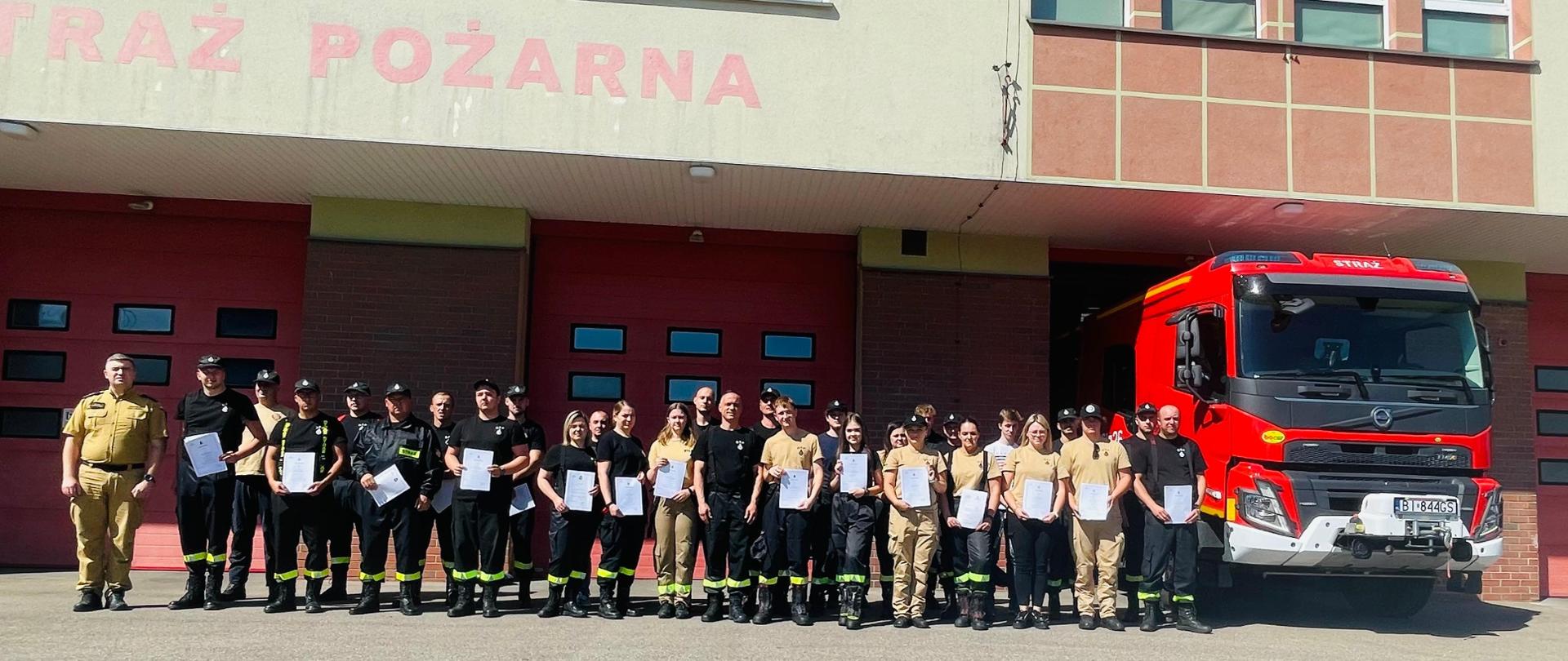 zdjęcie grupowe uczestników szkolenia wraz z uzyskanymi zaświadczeniami na tle budynku komendy miejskiej PSP w Łomży