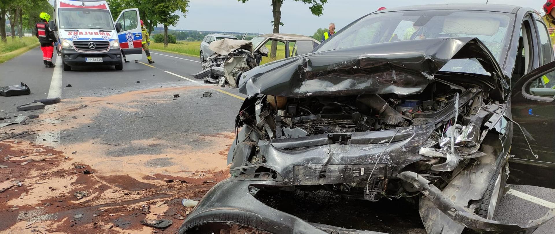 Widok na zniszczony przód pojazdu marki Peugeot. Na drugim planie karetka oraz drugi uszkodzony pojazd.
