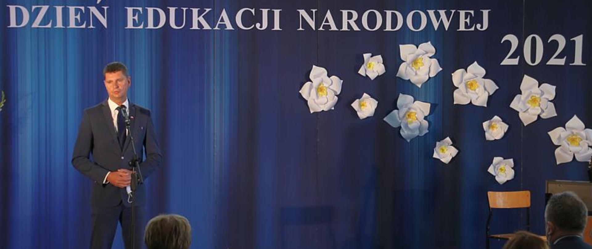 Wiceminister Dariusz Piontkowski gościem Dnia Edukacji Narodowej w Suwałkach, wiceminister Dariusz Piontkowski przemawia, stoi przed mikrofonem, z tyłu napis Dzień Edukacji Narodowej 2021.