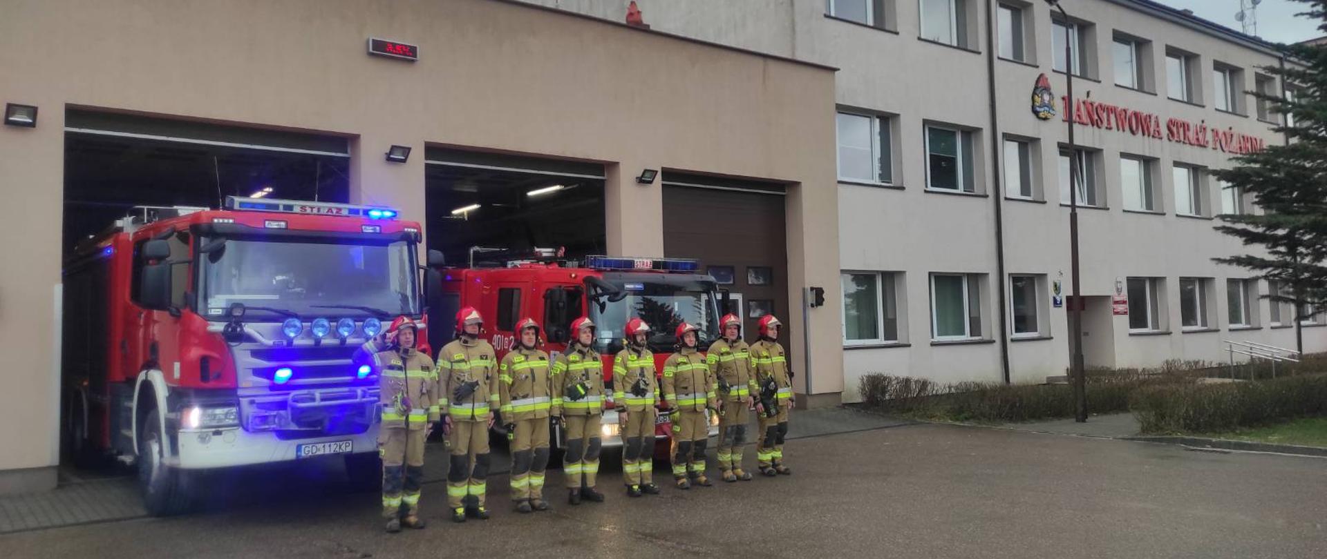 Na zdjęciu widać strażaków ustawionych w szyku na tle samochodów pożarniczych ubranych w ubrania specjalne podczas oddawania hołdu poległym.