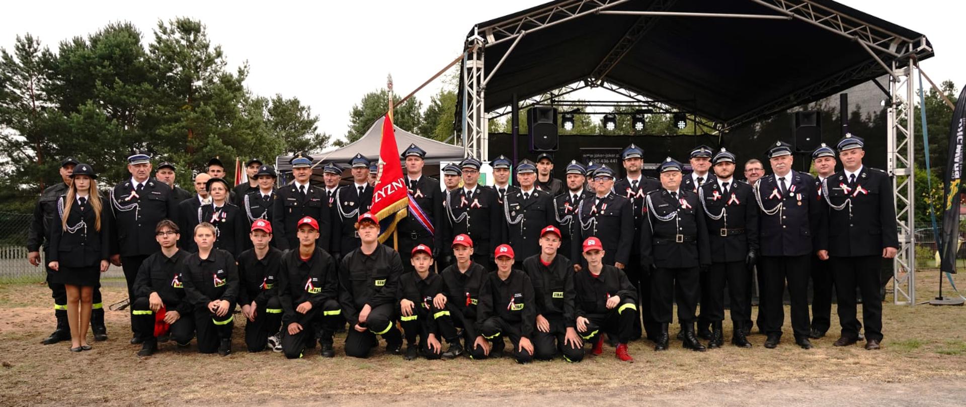 Uczestnicy uroczystości, w tym strażacy, młodzież i zaproszeni goście, ustawieni wspólnie do pamiątkowego zdjęcia grupowego.