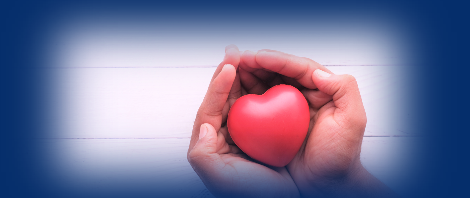 Złożone dłonie trzymające w środku gumowe serduszko. Wokół niebieskie tło