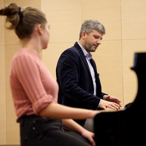 Grafika przedstawia osoby grające na fortepianie