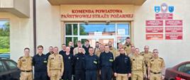 Zdjęcie grupowe uczestników szkolenia po egzaminie na tle wejścia głównego do budynku komendy powiatowej