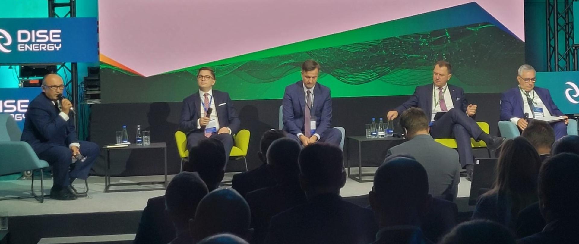 VII Kongres Energetyczny DISE - 4 panelistów oraz moderator siedzą na krzesłach podczas dyskusji pt.: "Energetyka jądrowa - wyzwania regulacyjne". Przed nimi publiczność.
