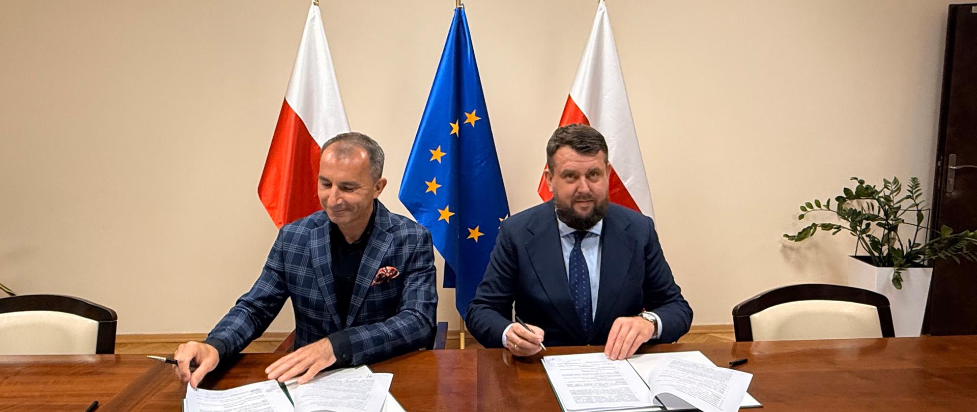 Dwaj mężczyźni przy biurku podpisują umowy