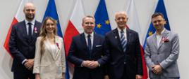 Zdjęcie grupowe z Wicewojewodą i innymi odznaczonymi. Na zdjęciu widoczne są flagi polski i unii europejskiej. 