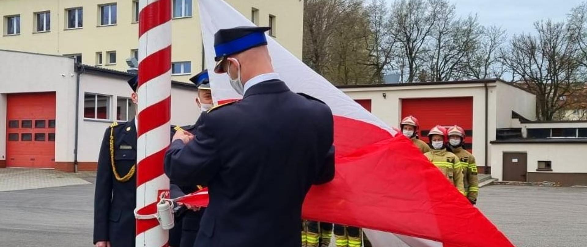Zdjęcie przedstawia funkcjonariuszy PSP podczas wciągana flagi na maszt. 