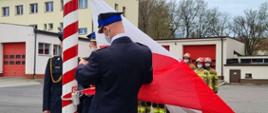 Zdjęcie przedstawia funkcjonariuszy PSP podczas wciągana flagi na maszt. 