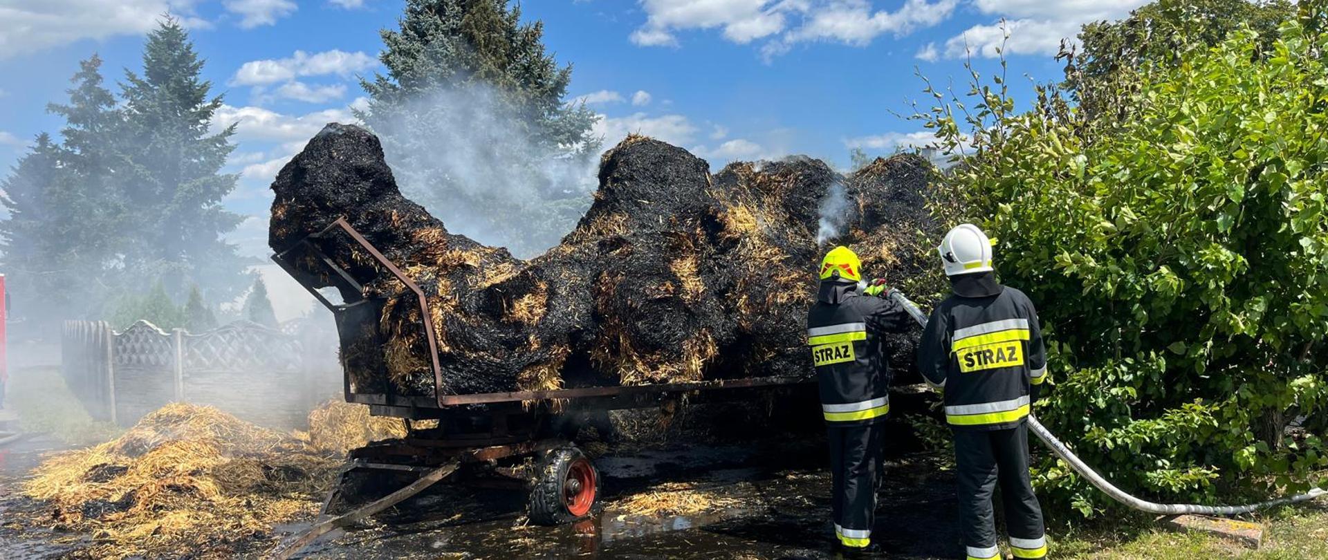 Spalona przyczepa z balotami słomy oraz strażacy podczas działań gaśniczych