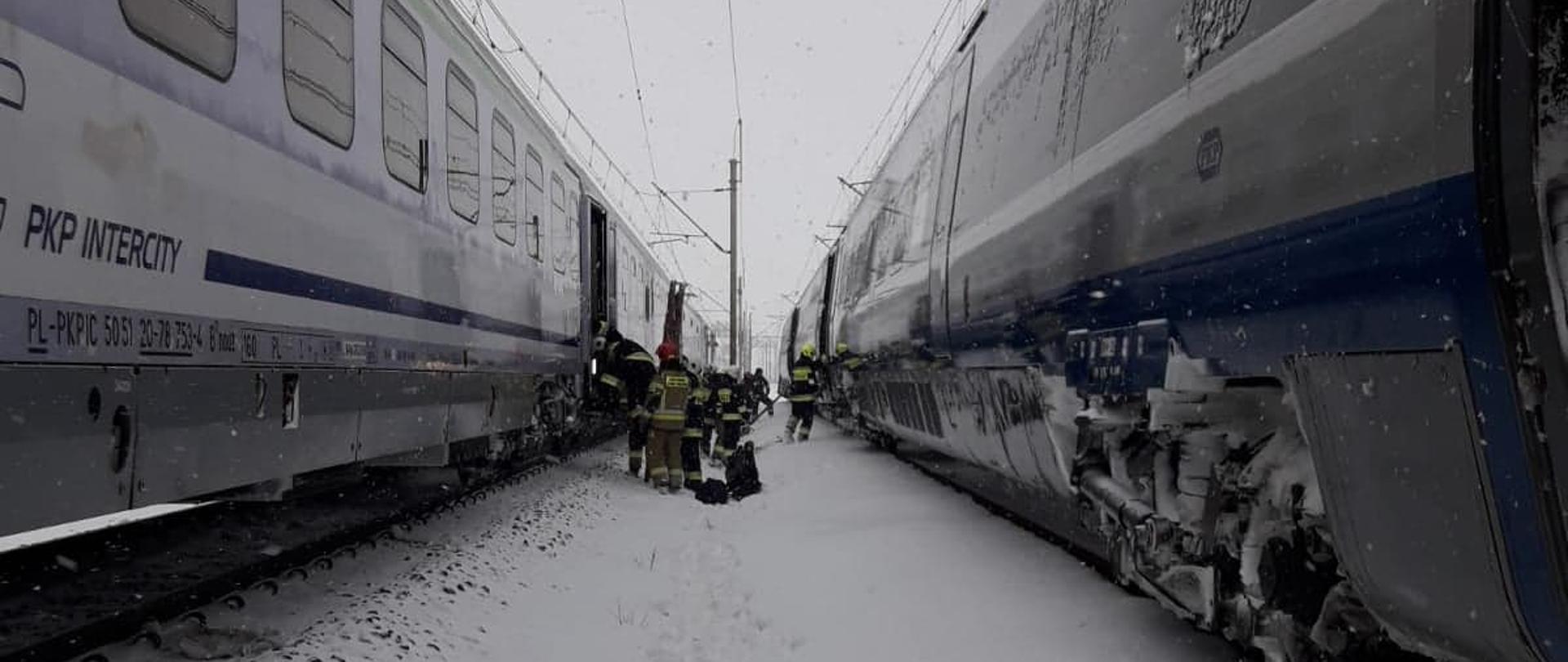 Strażacy w śniegu między torowiskami ewakuują pasażerów z jednego pociągu relacji Warszawa Wschodnia – Przemyśl Główny do drugiego podstawionego na równoległym torze relacji Warszawa Wschodnia - Zakopane.