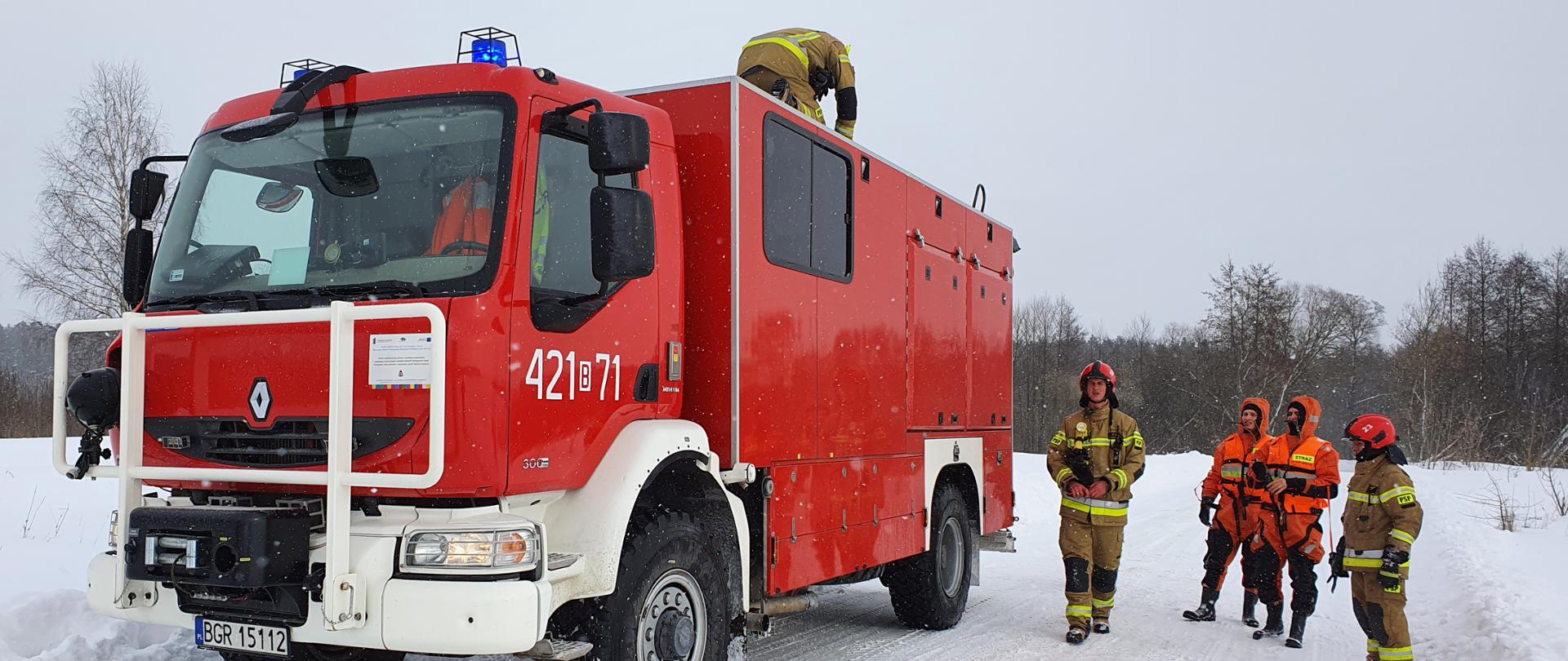 Na zdjęciu samochód ratownictwa wodnego. Obok stoją strażacy PSP w ubraniach typu nomex oraz ubraniach do ratownictwa lodowego.