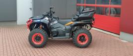 Nowy pojazd typu quad zakupiony dla Komendy Powiatowej Państwowej Straży Pożarnej w Brzezinach. Pojazd koloru czarnego z czerwonymi felgami, zdjęcie zrobione na placu komendy, za pojazdem widać budynek komendy.