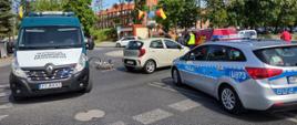 Od lewej: oznakowany furgon wielkopolskiej Inspekcji Transportu Drogowego stoi na środku skrzyżowania i zabezpiecza miejsce potrącenia rowerzystki przez kierującego samochodem osobowym. Obok leży przewrócony rower, stoi auto osobowe i oznakowany radiowóz Policji.