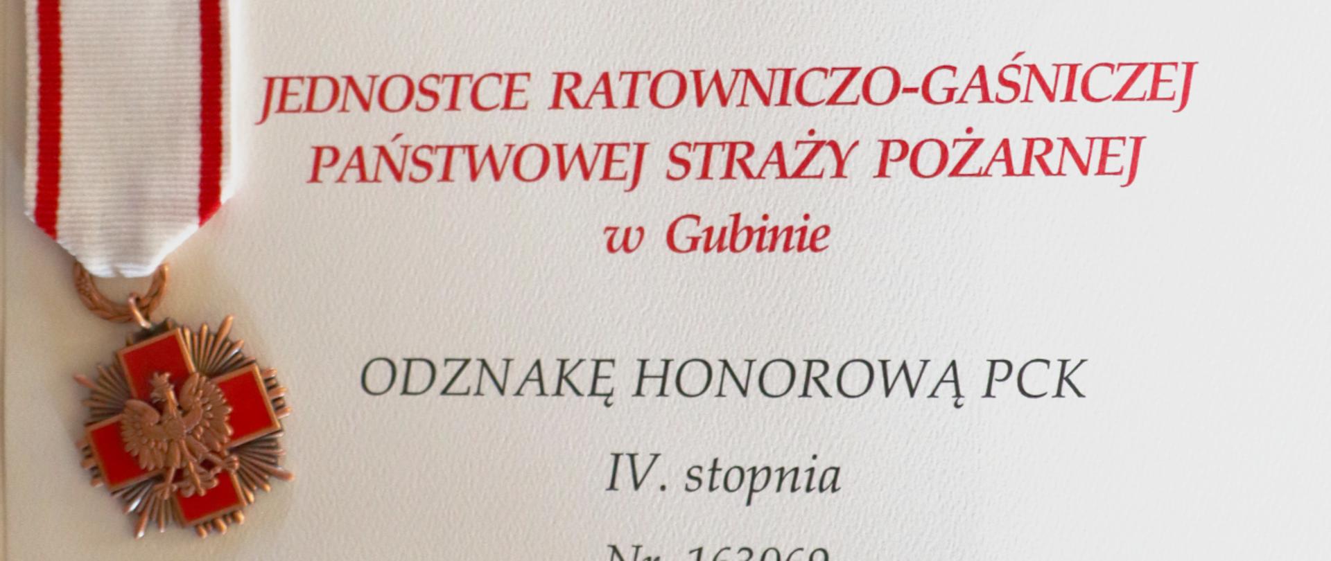 Zdjęcie przedstawia dokument informujący o nadaniu Jednostce Ratowniczo-Gaśniczej Państwowej Straży Pożarnej z Gubina Odznakę Honorową Polskiego Czerwonego Krzyża IV stopnia.