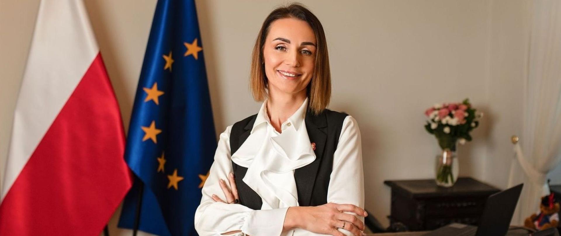 Kobieta na tle flag polskiej i unijnej składa życzenia noworoczne. Gabinet wojewody 