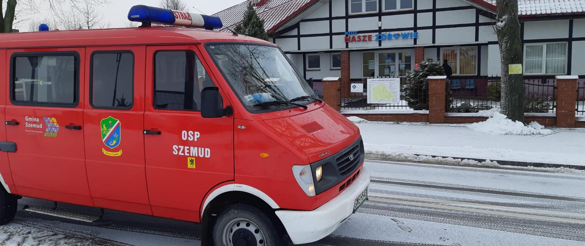 Zdjęcie przedstawia samochód ochotniczej straży pożarnej stojący pod punktem szczepień.