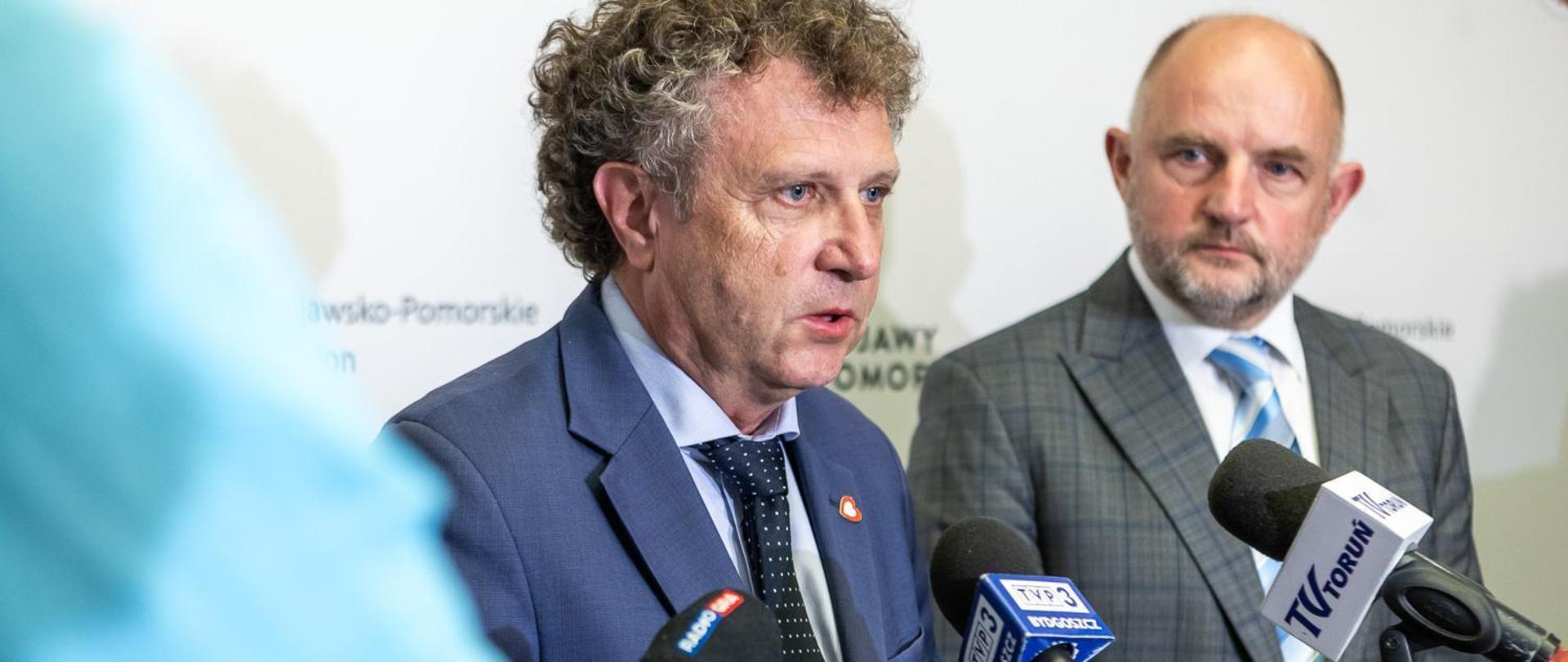 Dwie osoby stoją obok siebie przed mikrofonami.