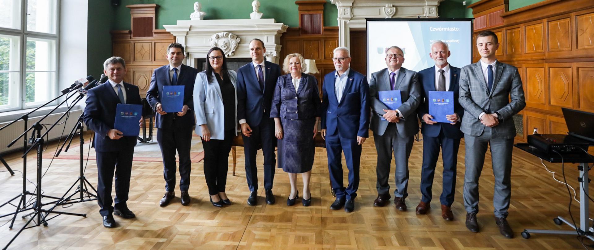 W sali muzealnej grupa osób pozuje do zbiorowego zdjęcia