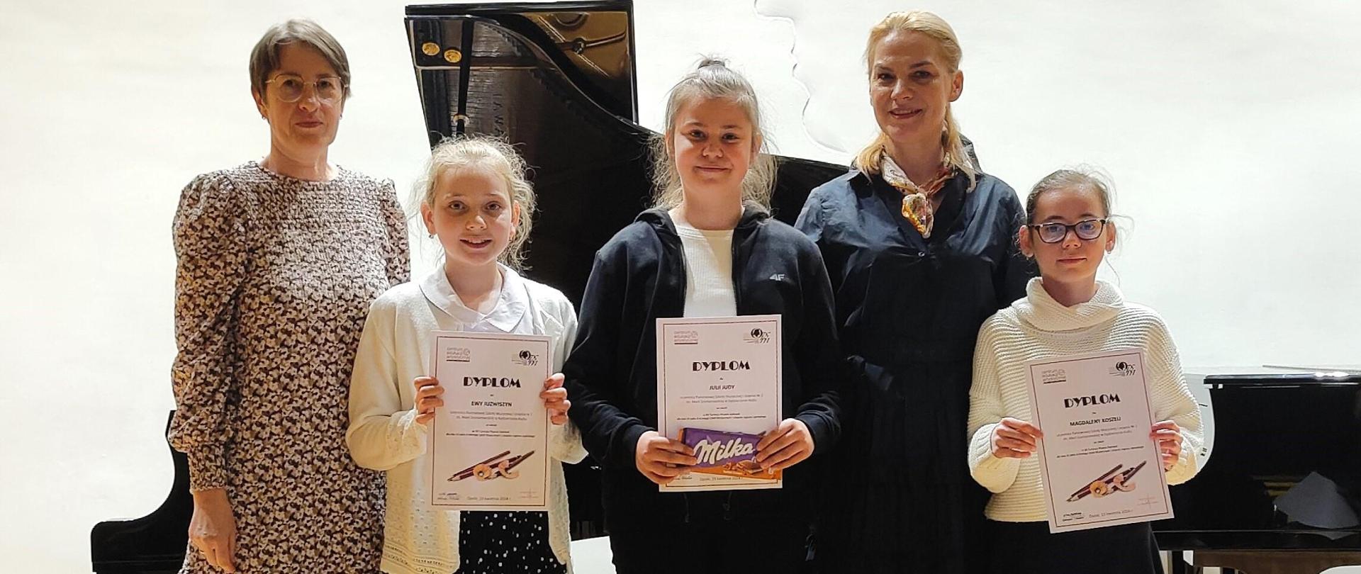 Na scenie stoją 3 uczennice z dyplomami w rękach, obok nich stoi nauczycielka Małgorzata
Meyse i dr hab. Agnieszka Chenczke-Orłowska