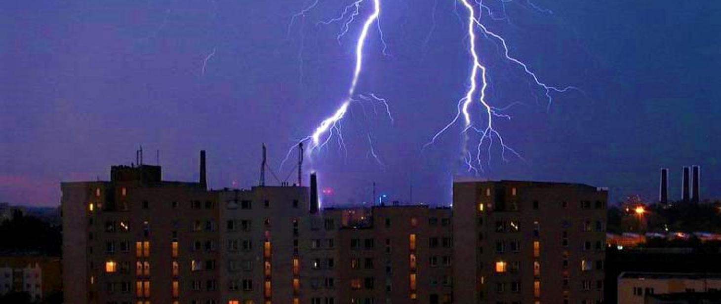 Błyskawice podczas burzy na tle budynków.