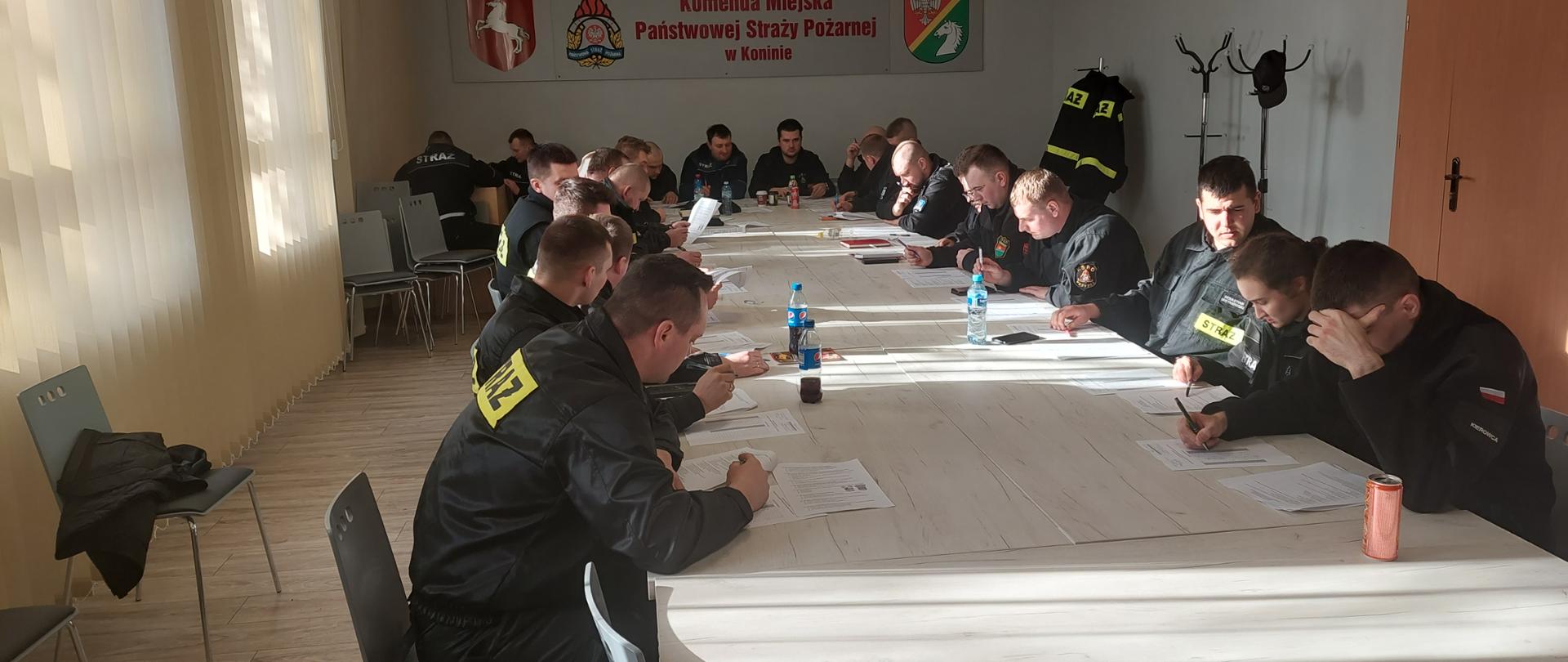 Zdjęcie przedstawia druhów OSP siedzących w świetlicy Komendy podczas szkolenia naczelników OSP. Druhowie siedzą przy stołach i rozwiązują testy. 