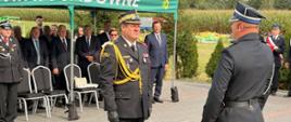 „Fragment uroczystości na placu przed remizą. Po lewej Komendant Komendant Wojewódzki PSP nadbryg. Artur Gonera, po prawej strażak (dowódca uroczystości) meldujący gotowość pododdziałów. W tle, pod namiotem Gminy Sadowne, widoczni zaproszeni goście.” 