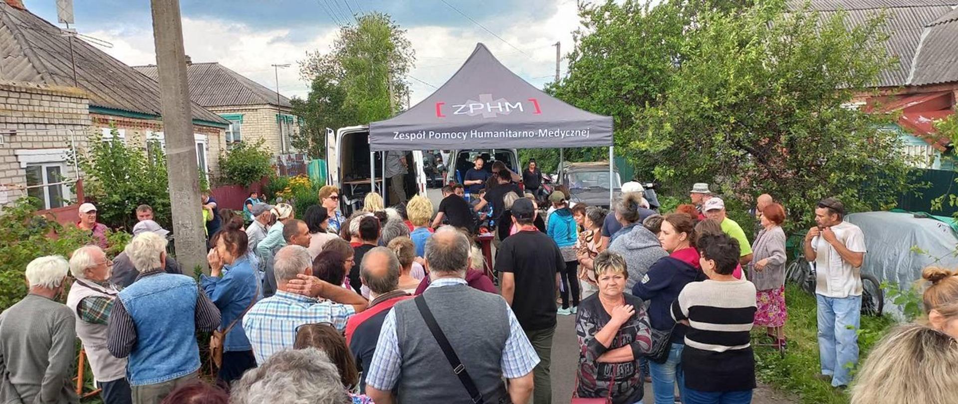 
Grupa ludzi stojąca przed namiotem pomocy humanitarnej
