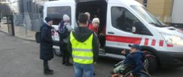 Zdjęcie przedstawia białego mikrobusa Państwowej Straży Pożarnej do którego wsiadają uchodźcy z Ukrainy.