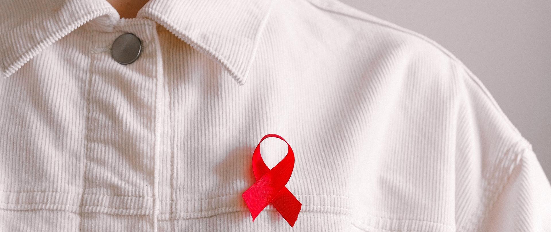 Mężczyzna w sztruksowej białej koszuli z wpiętą czerwoną wstążką symbolizującą poświęcenie i zaangażowanie w walkę z AIDS