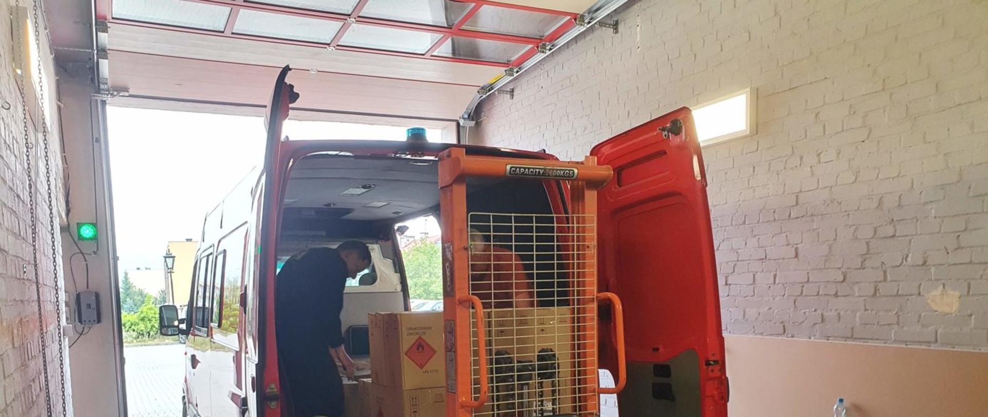 Załadunek środków ochrony indywidualnej na samochód należący do jednej z Ochotniczych Straży Pożarnych pomocą ręcznego wózka paletowego.