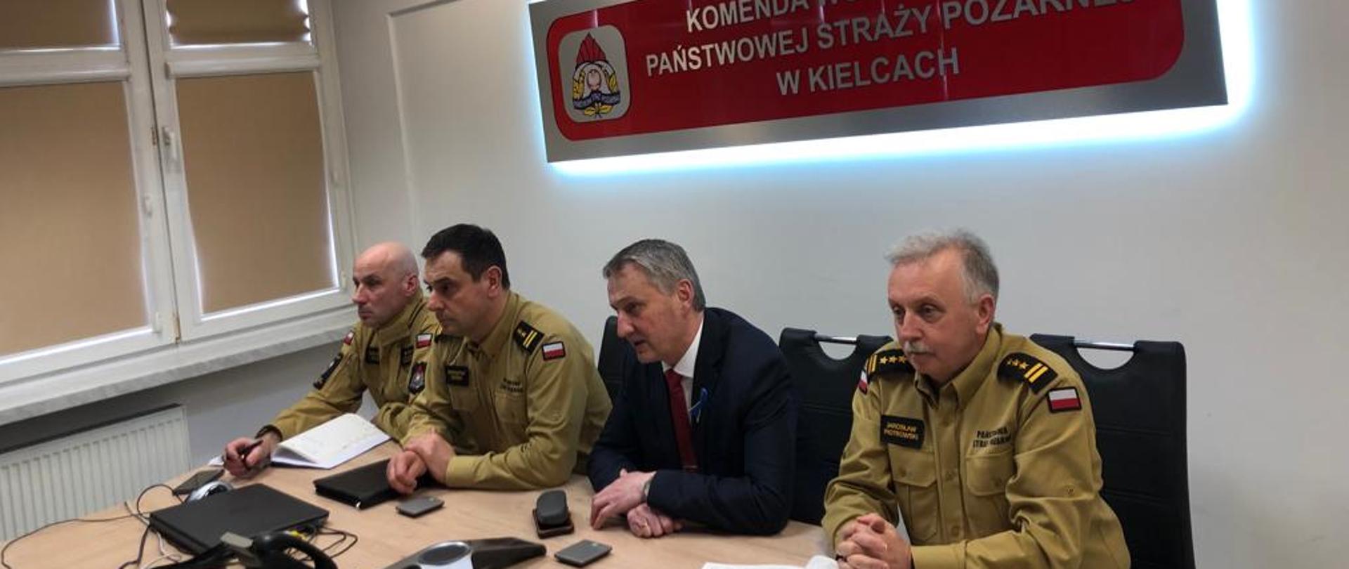 Na zdjęciu widzimy 4 mężczyzn. Trzech z nich jest w piaskowych mundurach PSP a jeden w garniturze ciemnym.