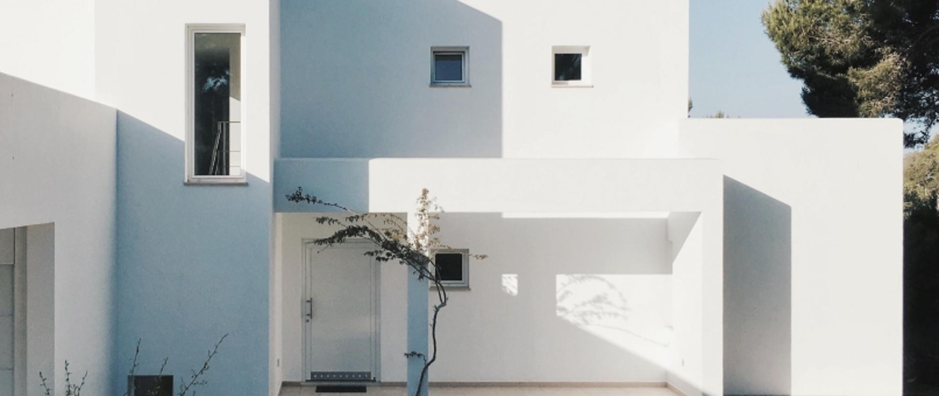 „Biały, nowoczesny dom z prostokątnymi oknami i drzewem przed wejściem.”