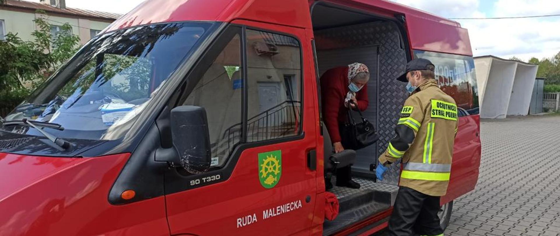 Strażak prowadzi kobietę do punktu szczepień