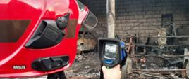 Strażak trzymający w ręku kamerę termowizyjną skierowaną na wnętrze warsztatu