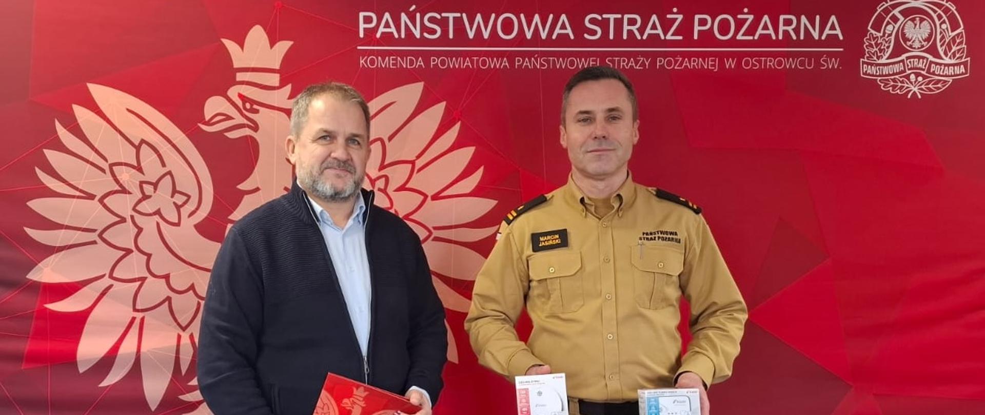 Na zdjęciu widoczny jest Komendant Powiatowy Państwowej Straży Pożarnej w Ostrowcu Świętokrzyskim trzymający czujki oraz Prezes Zarządu Akademii Przedsiębiorczości.