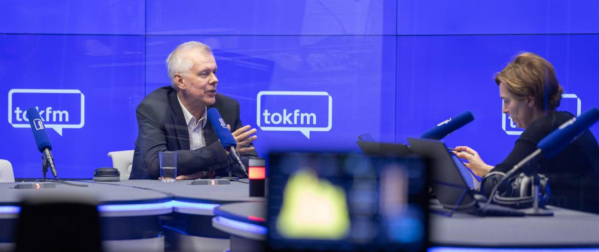 Minister Tomasz Siemoniak po lewej stronie, po prawej Karolina Lewicka. W tle granatowe tło z logiem TOK FM. Dwie osoby siedzą przy dużym, szarym stole. Na pierwszym planie rozmazany monitor. 