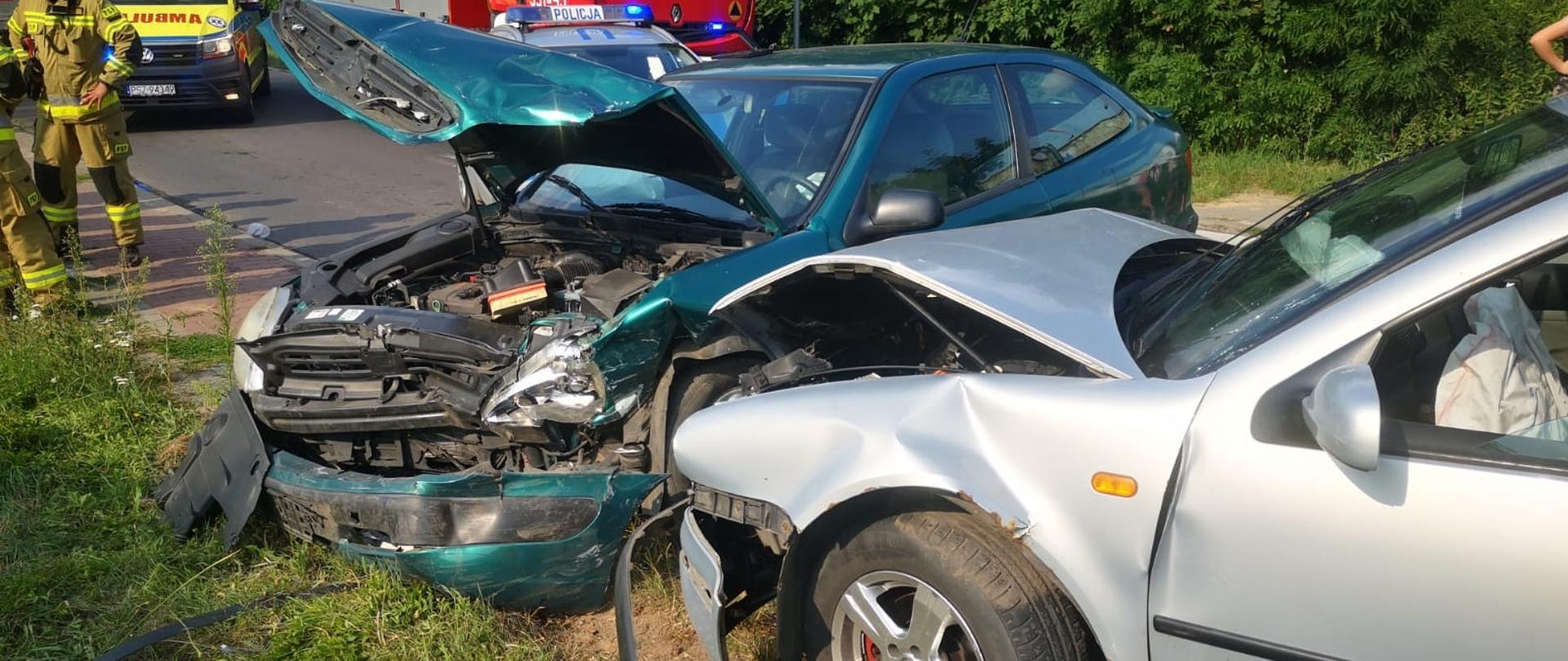 Widać dwa uszkodzone samochody, w oddali samochód strażacki