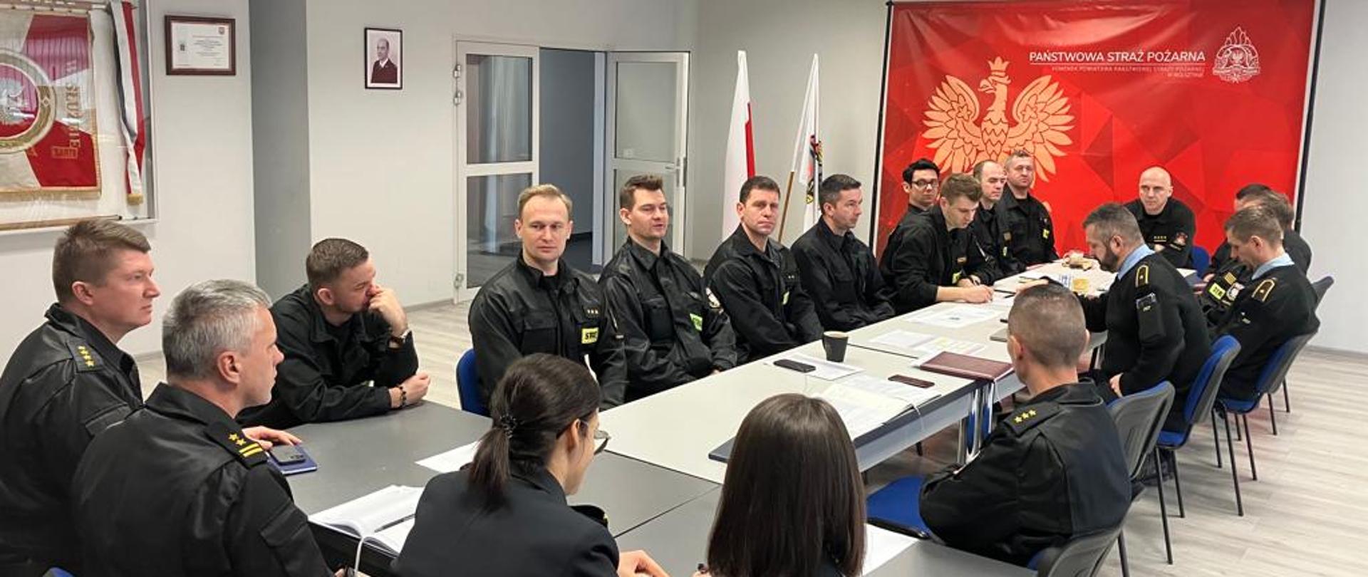 Funkcjonariusze siedzą przy stole i omawiają tematy bierzące. W tle czerwony baner PSP.